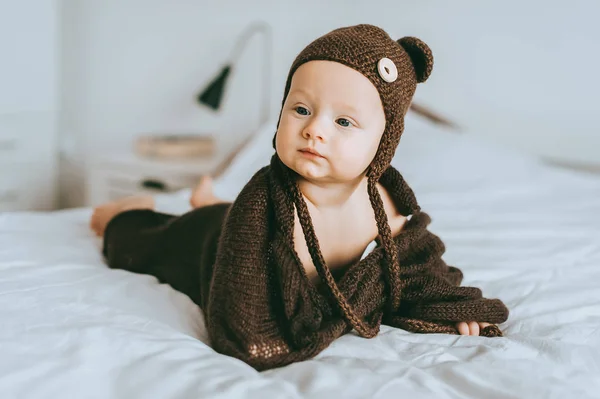 Criança infantil em chapéu de malha marrom e cobertor na cama olhando para longe — Fotografia de Stock