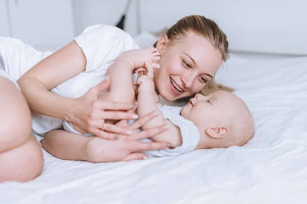 Sonriente joven madre y su bebé en la cama jugando en la cama en casa - foto de stock