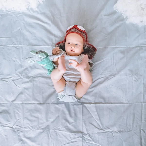Vue du dessus de l'enfant en bas âge en bonnet pilote tricoté jouant avec l'avion jouet au lit — Photo de stock