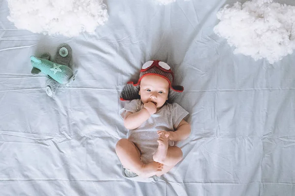 Top view of adorable infant child in pilot hat with toy plane surrounded with clouds made of cotton in bed — Stock Photo