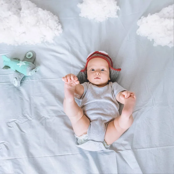Vista superior del niño en sombrero piloto con avión de juguete rodeado de nubes de algodón en la cama - foto de stock