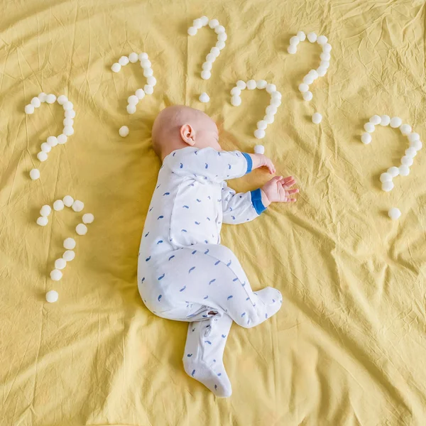 Вид сверху на младенца в окружении вопросительных знаков из ватных шариков, спящих на боку кровати — стоковое фото