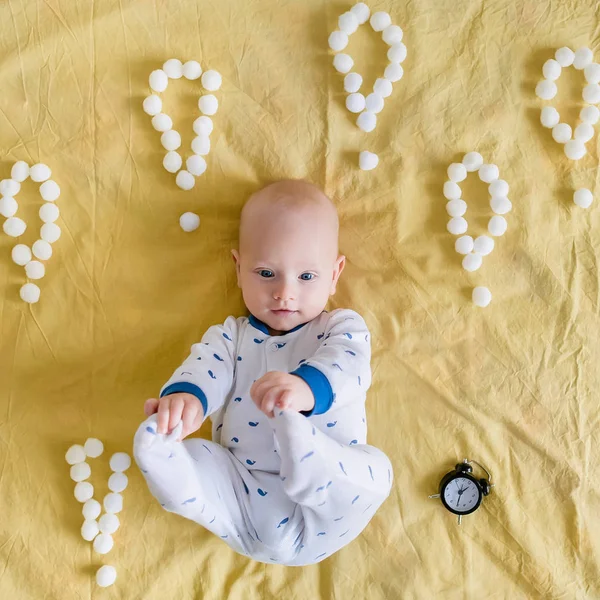 Vue de dessus de l'enfant en bas âge et réveil entouré de points d'exclamation en boules de coton le matin au lit — Photo de stock