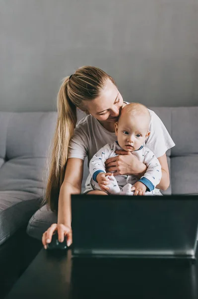 Mãe jovem e criança infantil usando laptop juntos enquanto sentados no sofá em casa — Fotografia de Stock