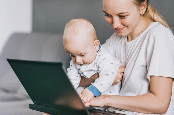 Sonriente madre sosteniendo niño pequeño y usando el ordenador portátil juntos - foto de stock