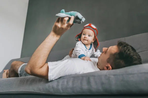 Father holding toy plane and playing with adorable infant child wearing knitted pilot hat — Stock Photo