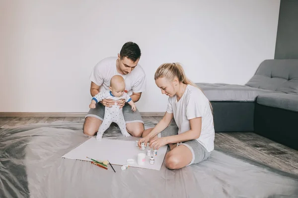 Feliz familia joven con hermoso niño pequeño pintando juntos en el suelo en casa - foto de stock