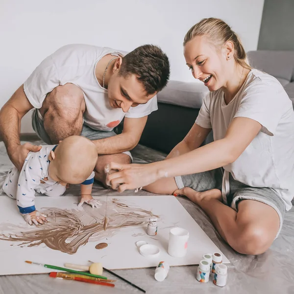 Hermosa familia joven feliz con lindo niño pequeño pintando juntos en el suelo en casa - foto de stock