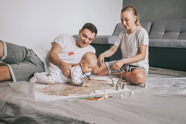 Young family with adorable infant child painting together on floor — Stock Photo