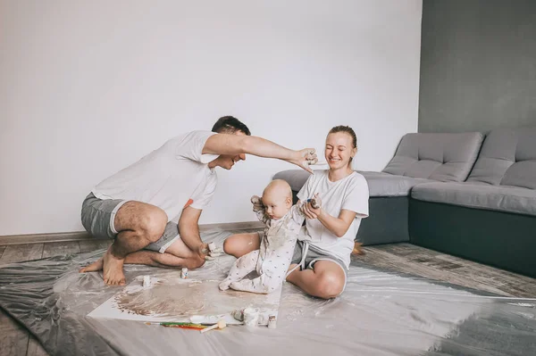 Feliz jovem família com bonito criança criança pintura juntos no chão — Fotografia de Stock