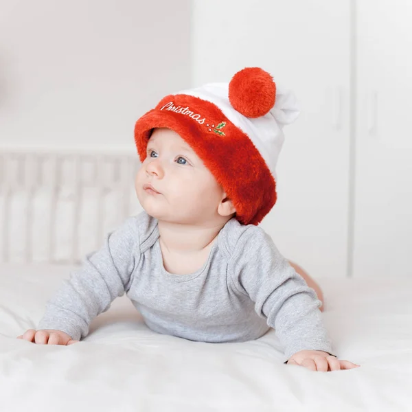 Ritratto di adorabile bambino neonato in cappello di Babbo Natale sdraiato sul letto e distogliendo lo sguardo — Foto stock