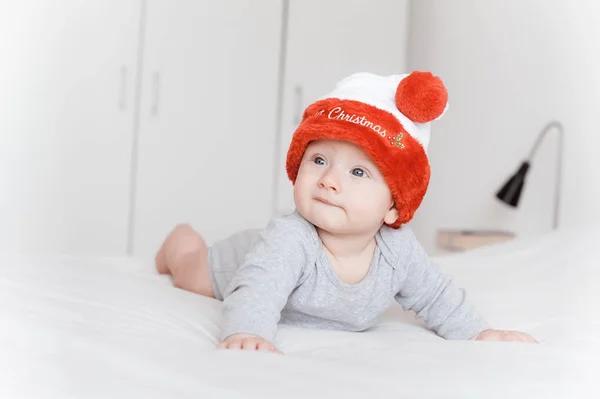 Ritratto del bellissimo bambino neonato in cappello di Babbo Natale sdraiato sul letto e distogliendo lo sguardo — Foto stock