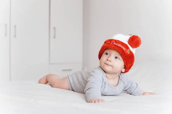 Porträt eines kleinen Säuglings mit Weihnachtsmütze auf dem Bett liegend und wegschauend — Stockfoto