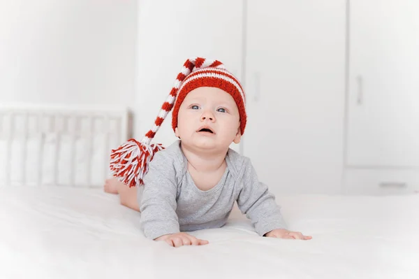 Portrait of adorable infant child in knitted hat lying on bed — Stock Photo