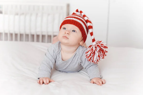 Portrait of cute infant child in knitted hat lying on bed — Stock Photo