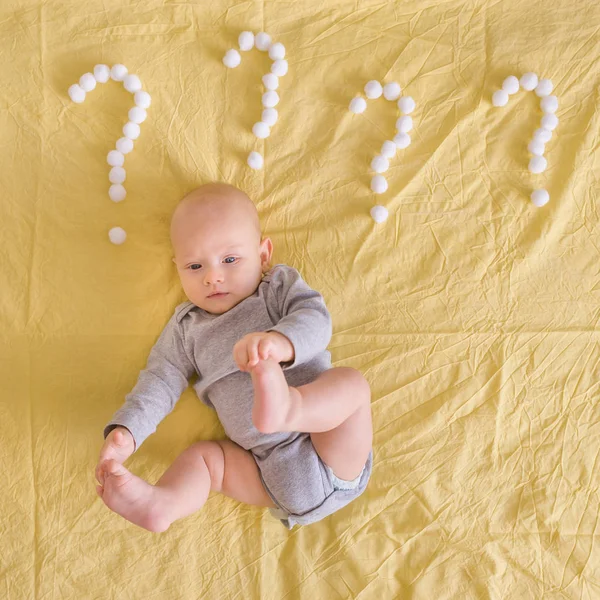 Сверху вид смешного младенца, лежащего в окружении вопросительных знаков из ватных шариков в постели — стоковое фото