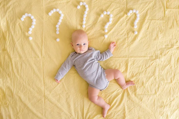 Top view of adorable infant child lying surrounded with question marks made of cotton balls in bed — Stock Photo