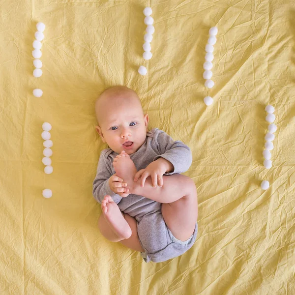 Vista superior de un niño pequeño y hermoso acostado rodeado de signos de exclamación hechos de bolas de algodón en la cama - foto de stock