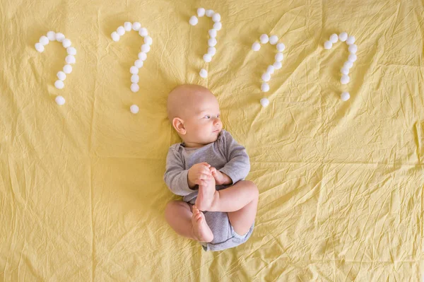 Vista dall'alto del bambino che giace circondato da punti interrogativi fatti di batuffoli di cotone a letto — Foto stock