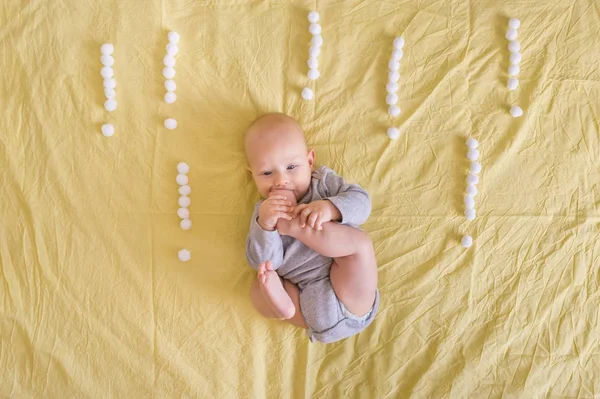 Vista superior de adorable niño divertido acostado rodeado de signos de exclamación hechos de bolas de algodón en la cama - foto de stock