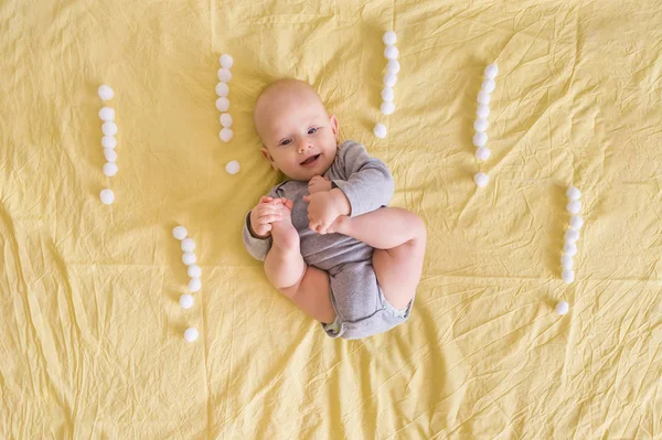 Очаровательный смешной ребенок лежит в окружении восклицательных знаков из ватных шариков в постели — стоковое фото