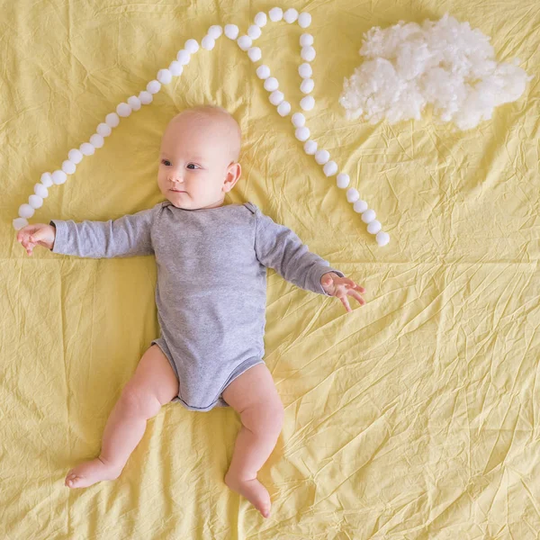 Top view of adorable infant child lying under house roof made of cotton balls and cotton cloud on bed — Stock Photo