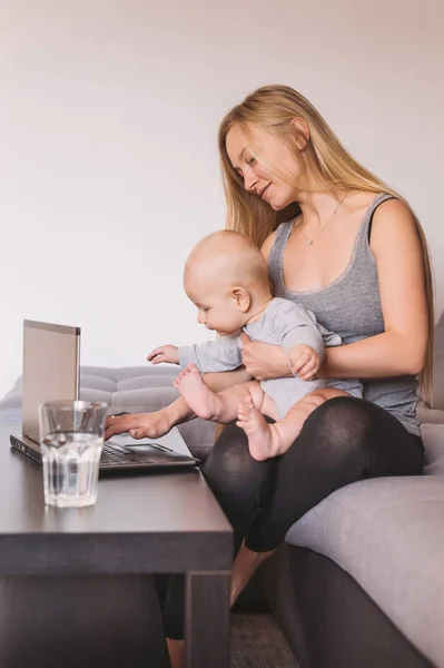 Усміхнена молода мати тримає чарівну дитину і використовує ноутбук — стокове фото