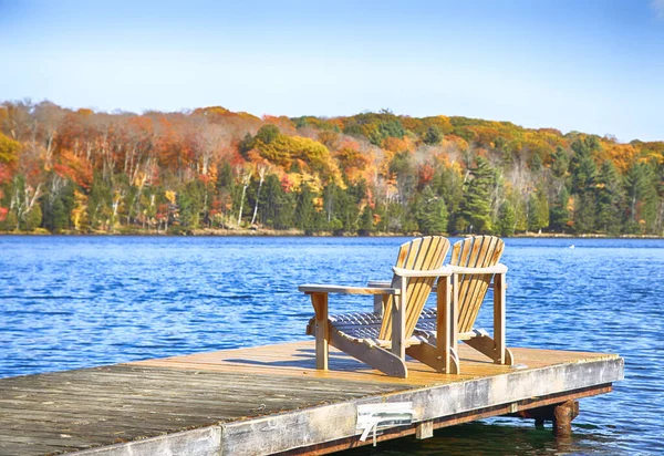 Dwa krzesła Muskoka na drewnianym pomoście nad błękitnym jeziorem — Zdjęcie stockowe