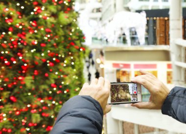 Adam alışveriş merkezinde Noel ağacının fotoğrafını çekiyor.