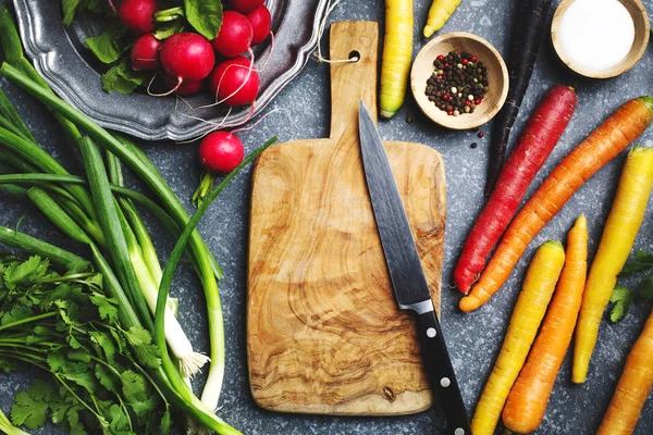 Verduras frescas de primavera alrededor de tabla de cortar de madera con cocina — Foto de Stock
