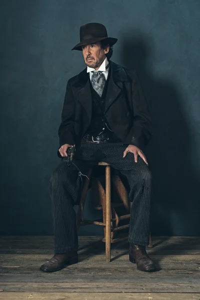 Mature man with revolver sitting on stool — Stock Photo, Image