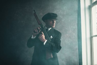 Pencereden dışarı bakarak silahla duran gangster