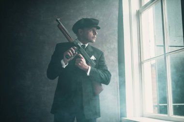 Pencereden dışarı bakarak silahla duran gangster