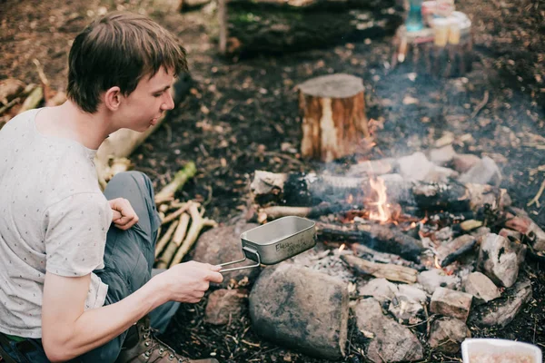 tourist putting frying pan into campfire