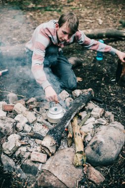 Adam kamp ateşi içine koyarak su ısıtıcısı 