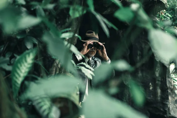 Человек с биноклем осматривает кусты — стоковое фото