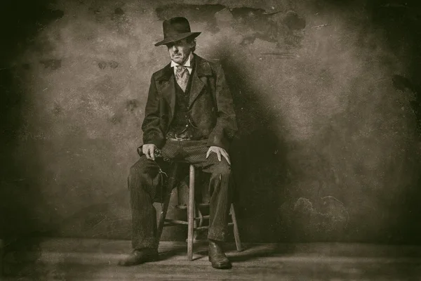 mature man with revolver sitting on stool