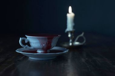 mum şamdan koyu ahşap masa üzerinde yanan ile kan beyaz çay bardağı dolu 