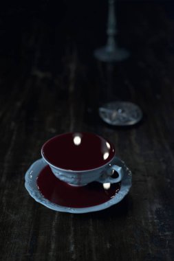 muska koyu ahşap masa üzerinde kanla dolu beyaz çay bardağı 