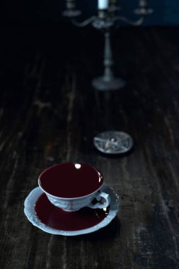 muska koyu ahşap masa üzerinde kanla dolu beyaz çay bardağı 