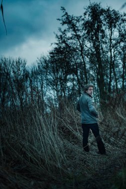 Sonbaharda sazlıklar arasında yürüyen ceketli bir adam..