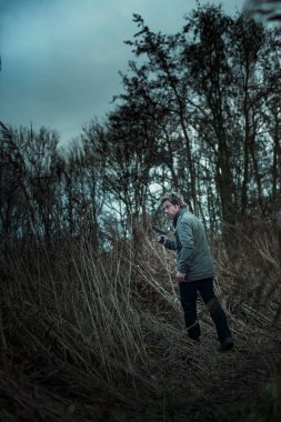 Bulutlu bir günde kamış arasında silahlı bir adam.