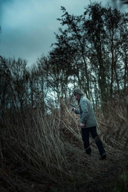 Bulutlu bir günde kamış arasında silahlı bir adam.