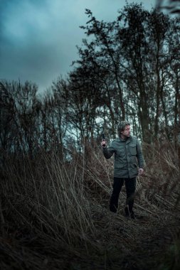 Bulutlu bir günde kamış arasında silahlı bir adam.