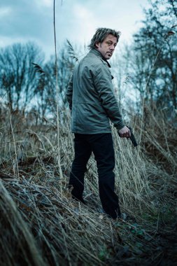 Bulutlu bir günde kamış arasında silahlı bir adam.