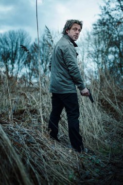 Bulutlu bir günde kamış arasında silahlı bir adam.