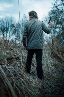Bulutlu bir günde kamış arasında silahlı bir adam.