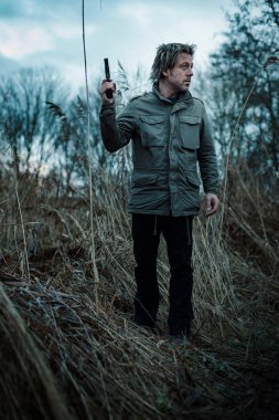 Bulutlu bir günde kamış arasında silahlı bir adam.
