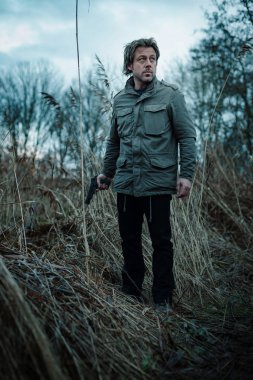 Bulutlu bir günde kamış arasında silahlı bir adam.