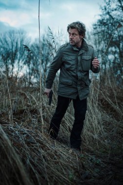 Bulutlu bir günde kamış arasında silahlı bir adam.